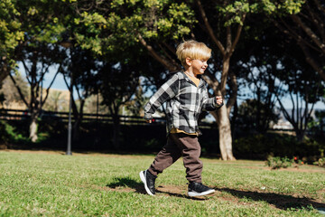 A little blond three-year-old boy runs in the park on the green grass