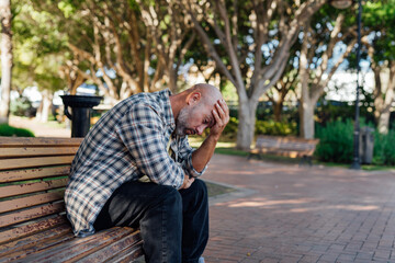 A man sits on a bench, holding his head in his hands. Distress, fear, emotions, problem