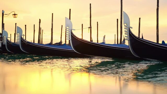 Gondolas in venice in the golden light of dawn with reflection on the stone shore