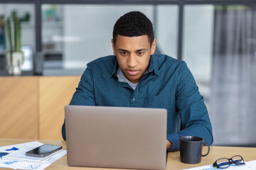 Concentrated African American man working using laptop while sitting in modern office