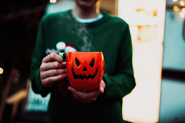 Portrait of candid authentic happy zoomer boy posing with jack lantern cup at halloween outdoor