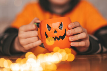 Portrait of candid authentic zoomer boy posing with jack lantern mug and sweets at halloween party