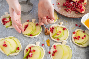 Child make apple shaped puff pastry with sliced apple and pomegranate seeds for Jewish holiday Rosh Hashanah.