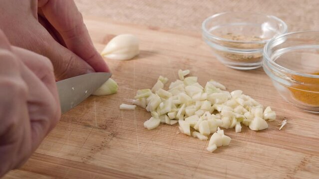 Chef hands chopping garlic on a wooden cutting board on a kitchen table, flat lay. Food preparation, marinated chicken recipe
