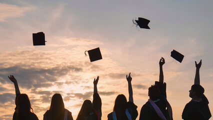 Student graduates toss their caps at sunset.