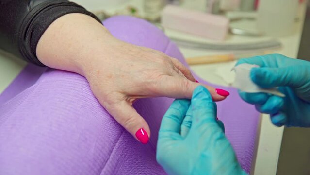 A beautician wipes her client's nails with a gauze pad after finishing painting,