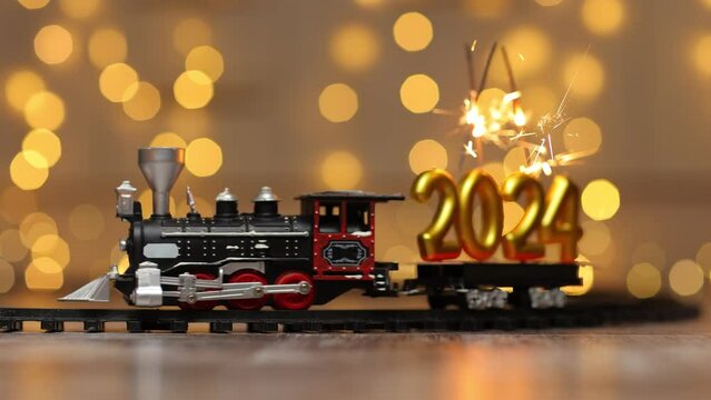 The train delivers the figures of the upcoming new year as cargo. The inscription 2024 sparkling with cheerful sparks.