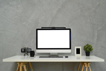 Stylish workplace with blank computer monitor, clock and houseplant on gray concrete background