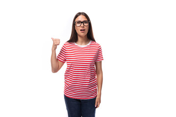 young cute brunette woman with glasses dressed in a striped t-shirt tells the news pointing her finger on a white background with copy space