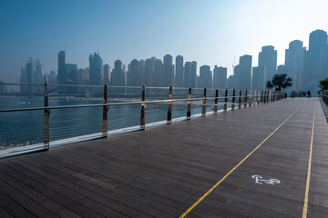 Dubai city silhouette and sea behind the timbered walking terrace bicycle lanes in Dubai blue waters island daylight misty hazy skies.
