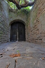 View of a wooden brown gate in a historic overgrown natural stone wall from the ground