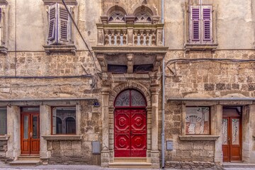 Image of a red entrance door to a residential building with a stone balcony and window with...
