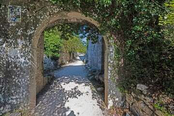 View through a curved overgrown gate onto an unpaved path in a medieval castle ruin
