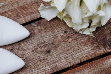 Beautiful wedding accessories, details, bride's set: beige shoes, bouquet of flowers with gold rings on a wooden surface.