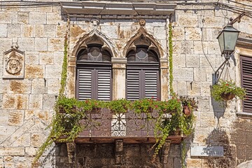 Image of a balcony with metal balustrade and doors with brown shutters on an antique façade