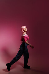 Stylish woman with pale pink hair wearing a pink jacket and jeans poses confidently against a pink background. Fashion advertising concept, individuality and confidence.