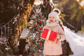 Little girl with a Christmas gift outdoors in winter on Christmas Eve. New Year background for holiday sale or promotion.