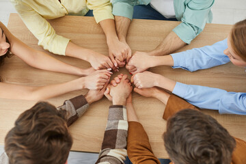 Group of people supporting each other. Team of young men and women friends sitting in circle around wooden table and holding hands together. Support, trust, connection, friendship, teamwork concept - obrazy, fototapety, plakaty