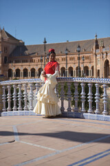 Naklejka premium Young black and South American woman in a beige gypsy flamenco suit, posing in a beautiful square in the city of Seville in Spain. Concept dance, folklore, flamenco, art. Vertical position.