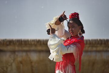 Young black and South American woman in a beige gypsy flamenco suit and red shawl, dancing with castanets in a beautiful square in the city of Seville in Spain. Concept dance, folklore, flamenco, art