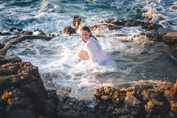 Young cheerful relaxed woman in a white shirt in a natural sea bath on the seashore. Thalassotherapy wellness concept