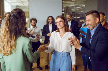 Partnership approval and teamwork. Female business colleagues congratulating each other on business achievements and excellent results at work. Women shake hands to applause of joyful business team. - obrazy, fototapety, plakaty