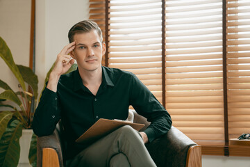 Portrait of happy and smiling male psychologist portrait sitting on arm chair in psychiatrist...