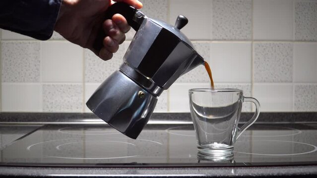 Male hand pouring coffee from moka  coffee maker in a transparent cup. Real time.