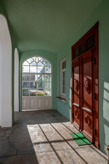 Natural Wood Front Door on light emerald background. Exterior with a large window and a shadow on the floor. Pope manor. Latvia, Baltic.