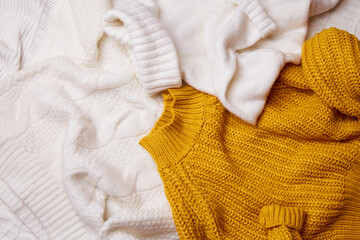 A pile of scattered knitted sweaters on the bed. Cozy autumn home background. Top view. 