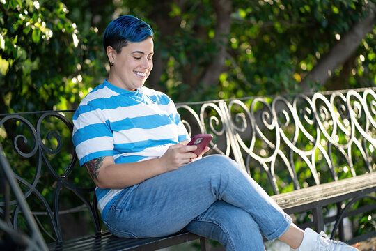 Androgynous Person Relaxing with Smartphone in Park - Powered by Adobe