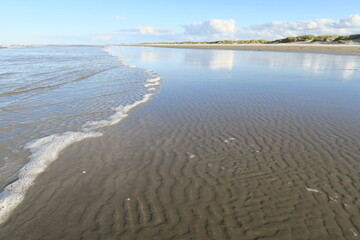 Auflaufendes Wasser am Strand der niederländischen Nordseeinsel Schiermonnikoog. Die Wolken spiegeln sich im Wasser der Nordsee. 