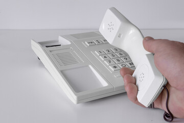 Desk phone 80s, 90s. Push-button dialing. White. Isolated on white table with a hand of man