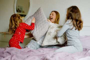Loving mother and two little sisters girls making pillow fight together. Happy family, woman and...