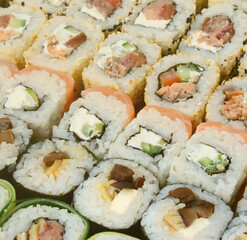 Close-up of a lot of sushi rolls with different fillings lie on a wooden surface. Macro shot of cooked classic Japanese food with a copy space.