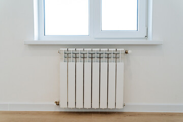 A heating radiator hangs under the window in a room, heating equipment in a residential building,...
