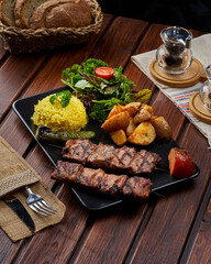 A plate of grilled kebab meat with potatoes and rice