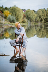 Portrait photo of a man sitting on a chair in the water, a guy in a yellow hat and a gray tracksuit.