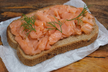 Salmon sandwich on textured paper over wooden background.  