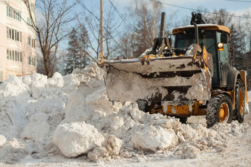 Fototapeta premium Snow removal on the street. Bulldozer removes snow in the city. Large blocks of snow.