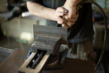 Guy in garage is repairing steel part. Man grinds iron.
