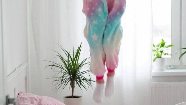 A girl in warm kigurumi pajamas is jumping on the bed.