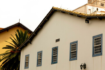 Parede branca, telhado de telha de barro e janelas com moldura de cor azul. 