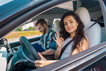 Happy young woman showing ok gesture while driving car during test drive. Male instructor filling out a report. Test drive, transportation, safety, education concept - obrazy, fototapety, plakaty