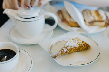 Sweet cannoli stuffed with cream and cup of black coffee for breakfast on a table in a cafe.
