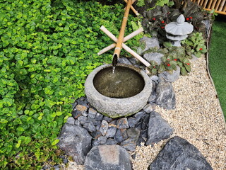 A samall Japanese garden  have plant Creeping Charlie and annual Carpet plant with red flowers as a ground cover, sprinkled with white pebbles. Border the garden with bricks and waterfall from bamboo 