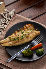 A plate of mackerel with boiled vegetables on a wooden floor