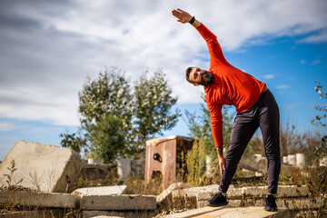 Adult man is exercising outdoor on sunny day. He is stretching his body.