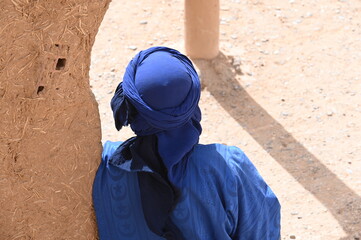 Ein Tuareg mit blauem Turban lehnt sich an die Wand einer Lehmhütte