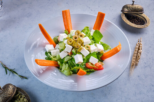 A blate of green salad with cheese and carrots on a gray background